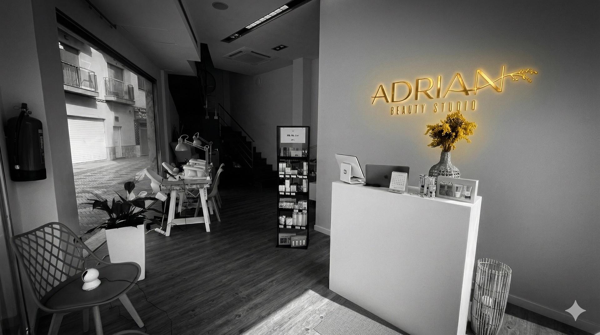 Recepción de Adrian Beauty Studio Gandía — mostrador blanco con el logo dorado iluminado y flores amarillas